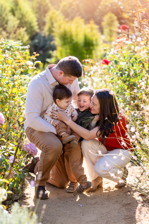 Parents crouch close around their two toddlers for a playful fall family portrait among the flowers.