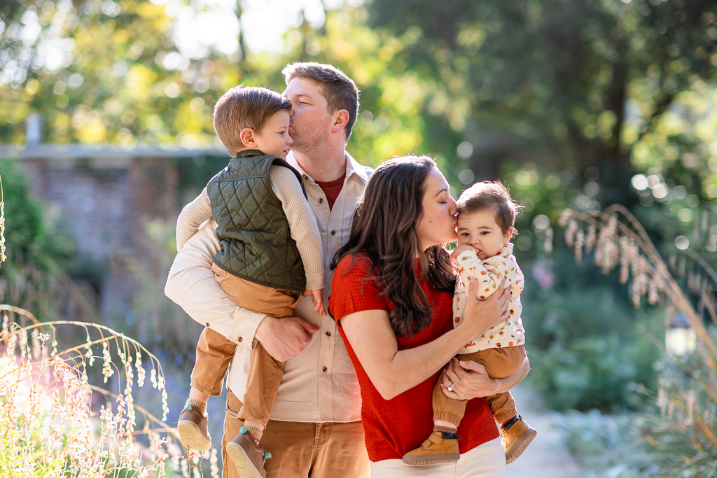The parents kiss their children in a tender family moment surrounded by Elizabeth Gamble Garden’s greenery.