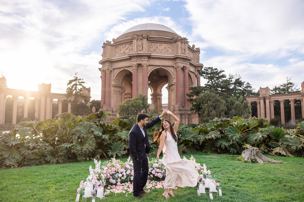 Beautiful romantic golden hour Palace of Fine Arts engagement shoot of a man twirling his laughing partner beside their floral proposal display